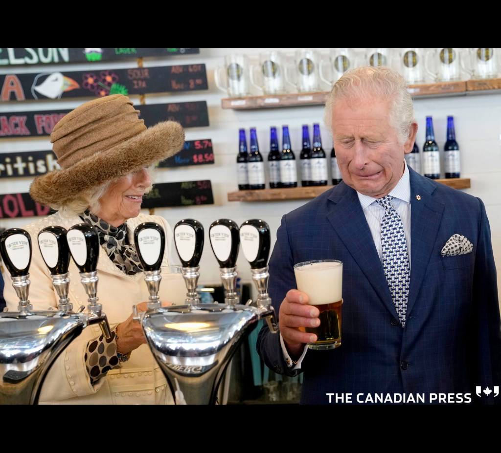 Prince Charles reacts to a bad pour of beer he made at the Quidi Vidi Brewery as Camilla, Duchess of Cornwall looks on during their Canadian Royal tour in St.John’s, Tuesday, May 17, 2022. THE CANADIAN PRESS/Paul Chiasson